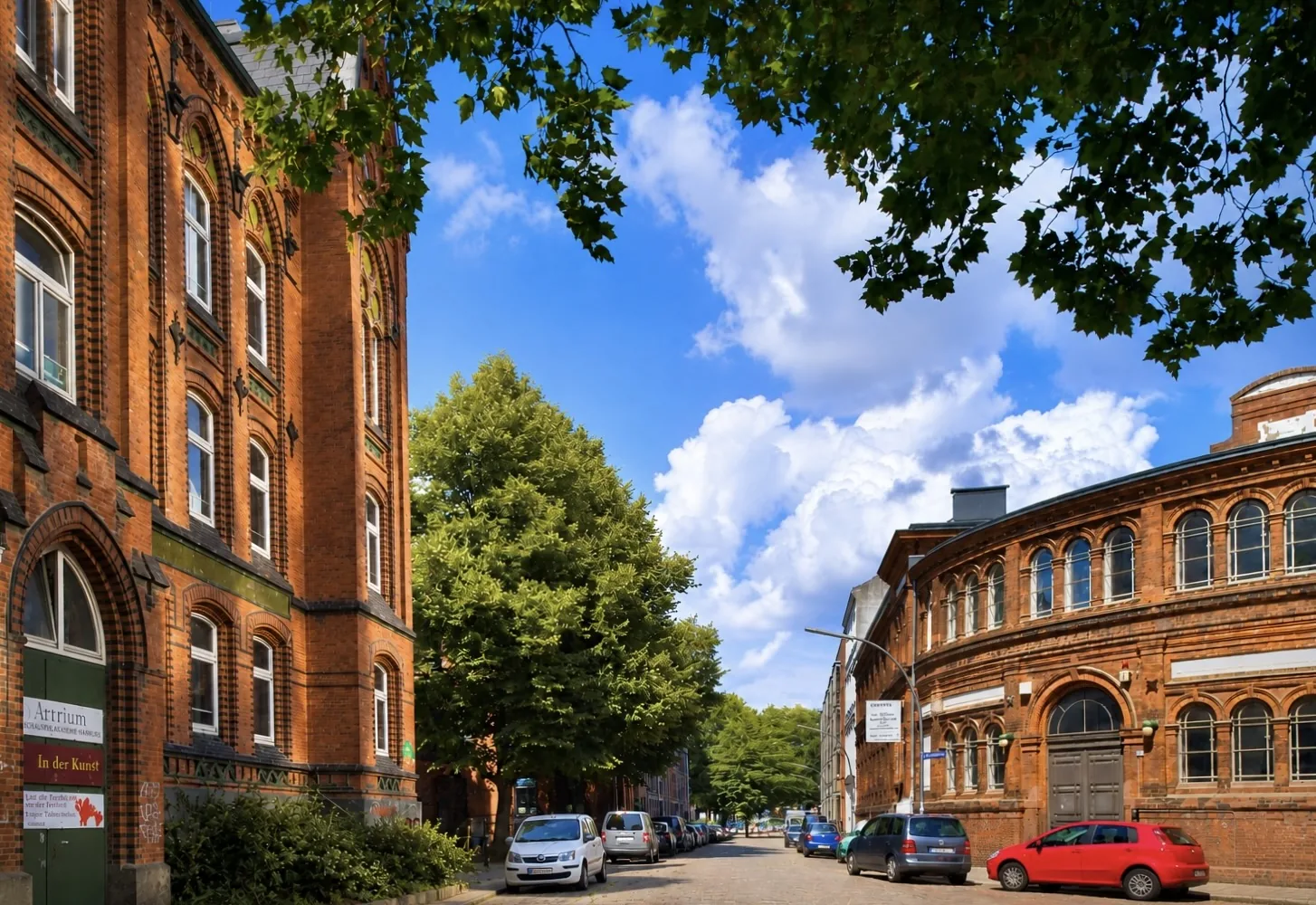 Backsteingebäude des Artrium in der Thedestraße in Hamburg-Altona, davor eine kopfsteingepflasterte Straße mit Bäumen und parkenden Autos