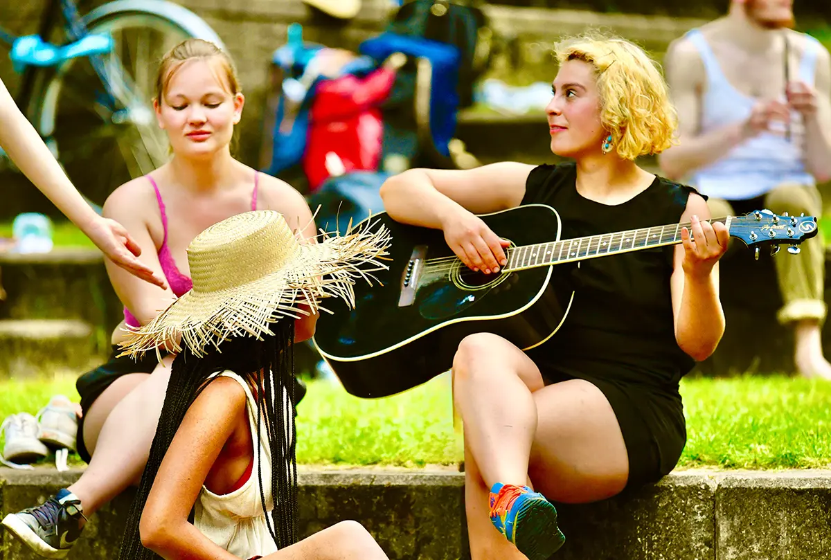 Zwei Teilnehmerinnen der Sommerakademie musizieren mit Gitarre und Sonnenhut im Park