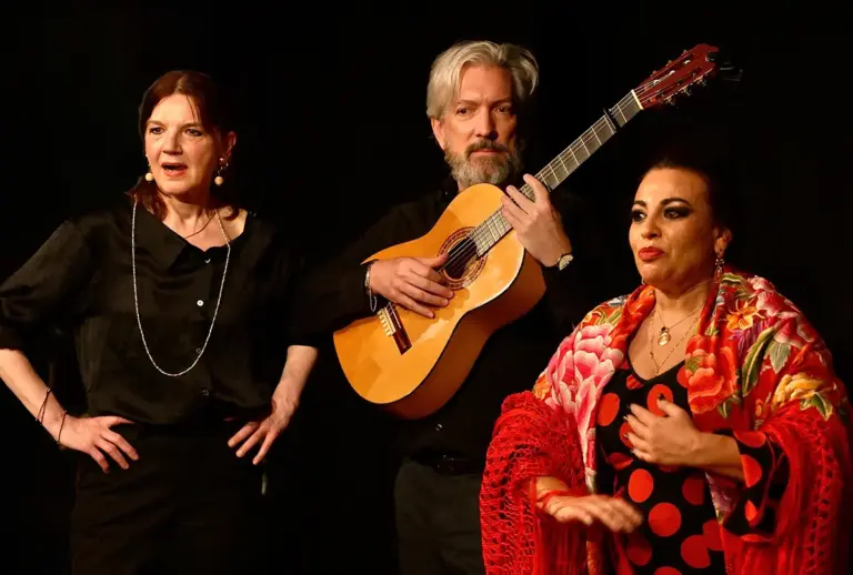Flamenco-Aufführung auf der Bühne: eine singende Frau, ein Gitarrist und eine Tänzerin im rot gepunkteten Kleid mit geblümtem Tuch.