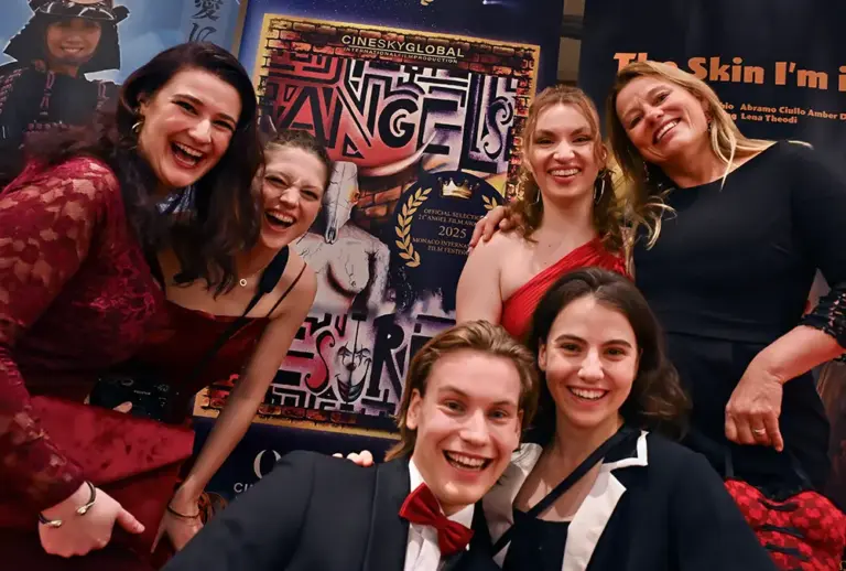 Fröhliche Gruppe des Artrium-Ensembles vor dem Plakat „Angels Desired" bei den Angel Film Awards des Monaco International Film Festival 2025.