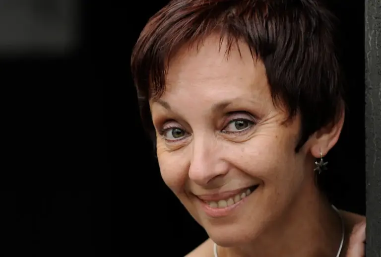 Porträt der lächelnden Dozentin Stela Korljan mit kurzen rotbraunen Haaren vor dunklem Hintergrund.