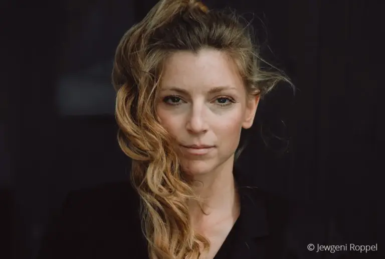 Porträt der Schauspieldozentin Isabell Giebeler mit gewelltem blondem Haar vor dunklem Hintergrund.