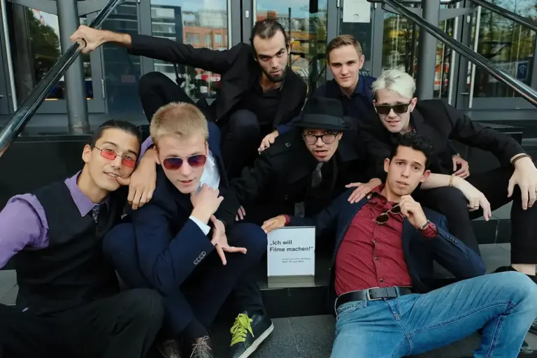 Gruppe junger Männer posiert lässig auf einer Treppe neben einem Schild mit der Aufschrift „Ich will Filme machen!".