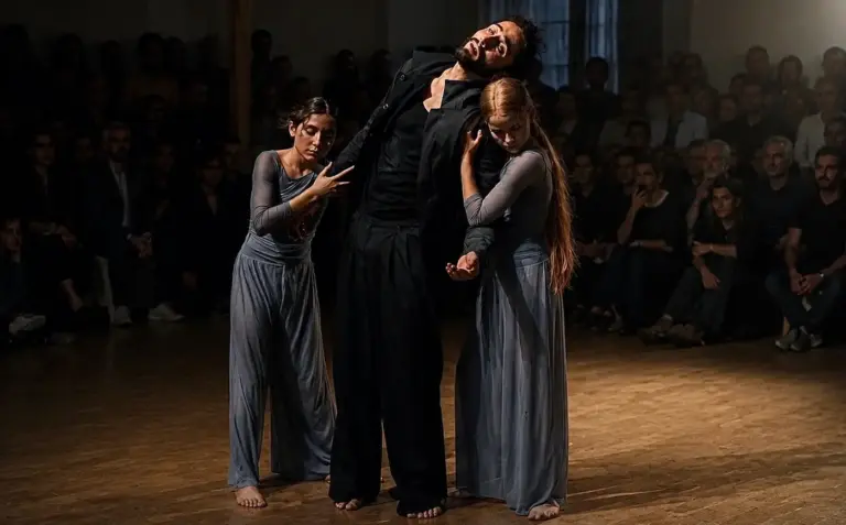 Tanztheater-Aufführung: drei Tänzer in einer ausdrucksstarken Pose in der Mitte des Raums, ringsum das dicht sitzende Publikum.