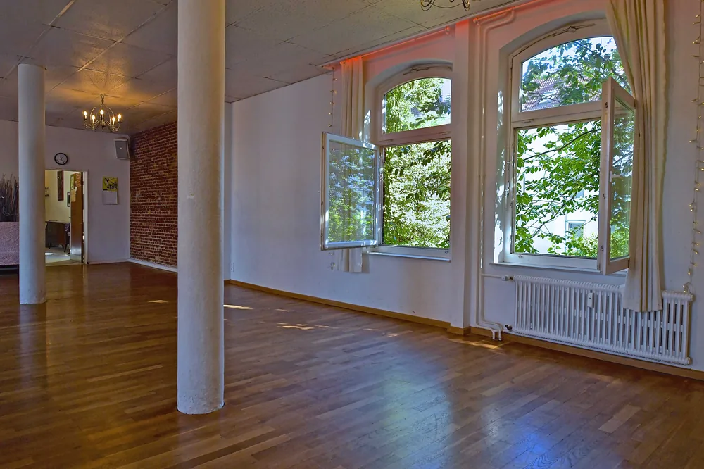 Großer Probenraum im Artrium mit Holzdielen, weißen Säulen, Bogenfenstern und freiliegender Backsteinwand