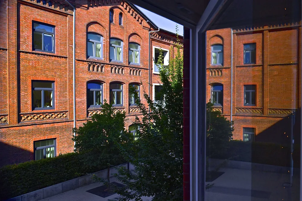Blick aus einem Fenster des Artrium auf den begrünten Backstein-Innenhof mit Bäumen und Rundbogenfenstern