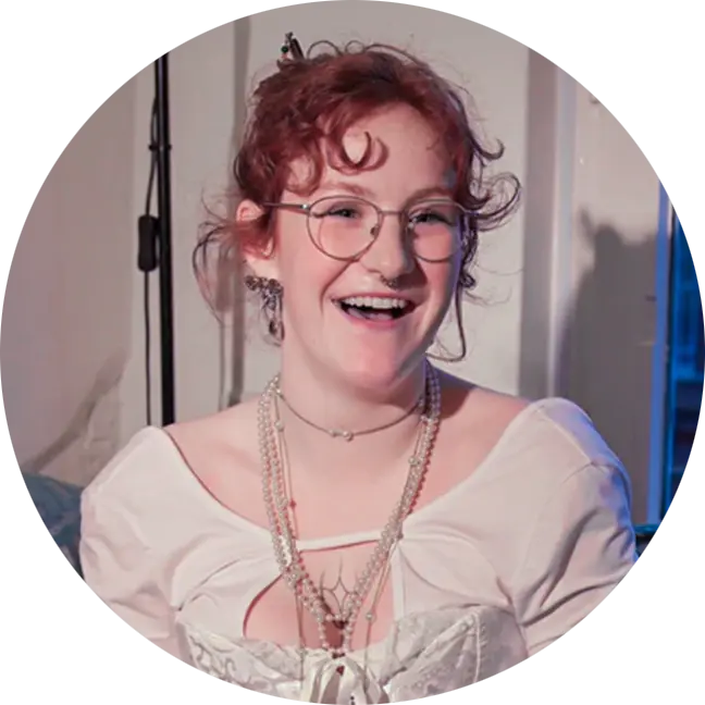 Portrait von Bente Rustike, lachend, mit roten Locken, runder Brille und Perlenketten