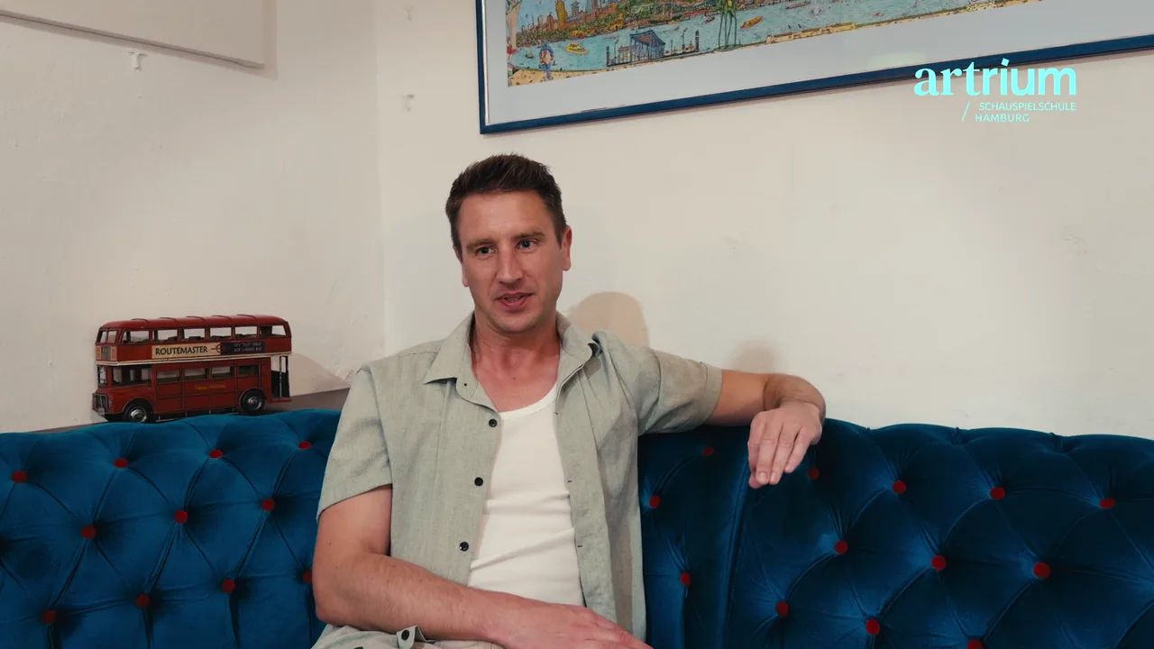 Frederik sitzt mit ausgestrecktem Arm auf dem blauen Sofa am Artrium und erzählt von seiner berufsbegleitenden Schauspielausbildung.