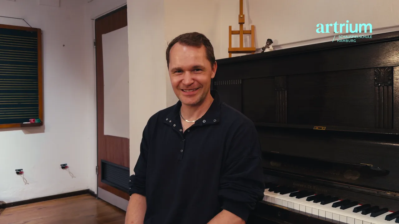 Johannes sitzt lächelnd vor dem Klavier am Artrium und erzählt von seiner berufsbegleitenden Schauspielausbildung.