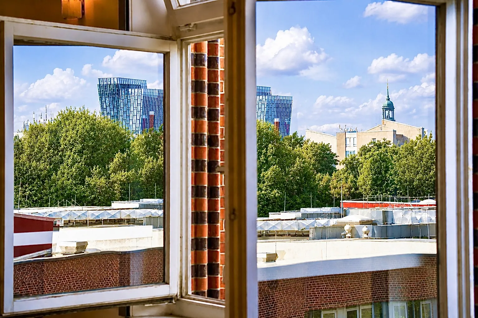 Blick aus einem geöffneten Fenster des Artrium über die Dächer von Hamburg-Altona, am Horizont Hochhäuser und ein Turm mit grüner Kuppel