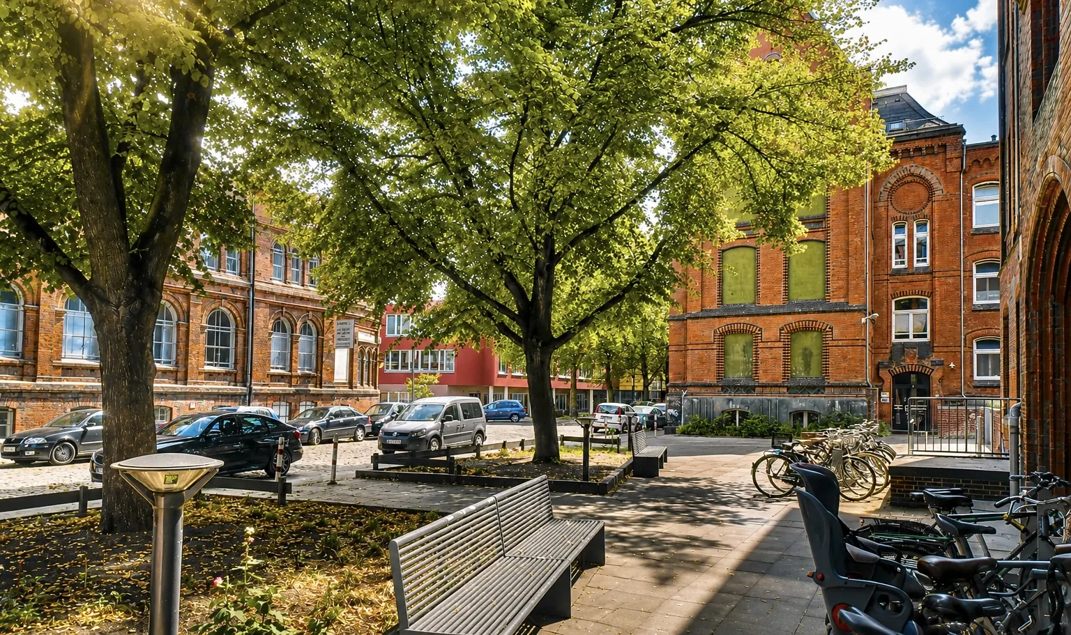 Begrünter Platz vor dem Artrium in der Thedestraße mit Bäumen, Sitzbank, Fahrradbügeln und Parkplätzen