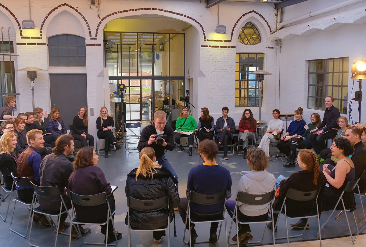 Das Ensemble sitzt im großen Loftraum in einem Stuhlkreis, hohe Fenster und weiße Backsteinwände