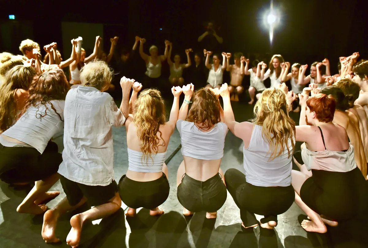 Ensemble der Schauspielschule Artrium steht im Kreis, alle halten sich an den Händen, warmes Bühnenlicht