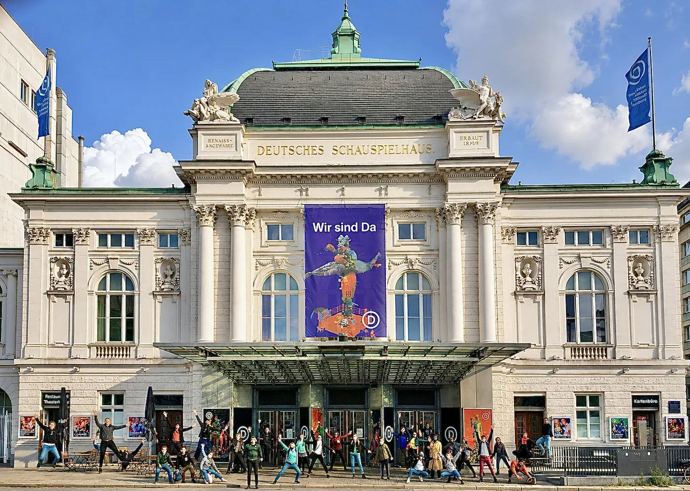 Ensemble des Artrium vor dem Deutschen Schauspielhaus in Hamburg, die Gruppe steht mit ausgestreckten Armen vor dem Eingang