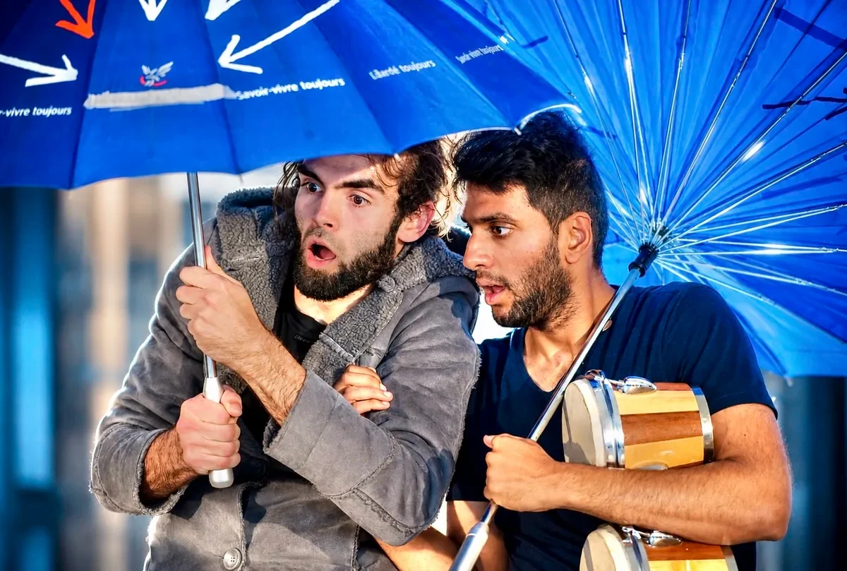 Zwei Spieler stehen erschrocken unter einem blauen Regenschirm, einer hält eine Trommel