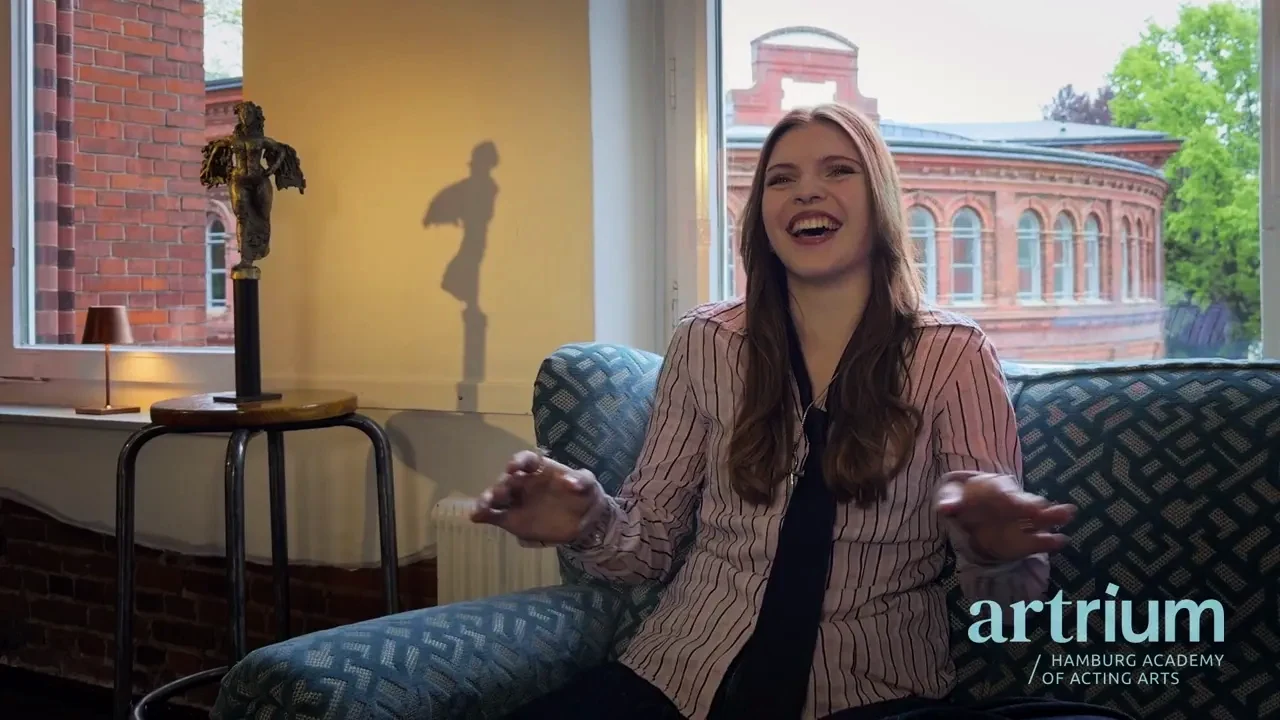 Lilly sitzt lachend auf einem Sessel am Fenster und erzählt von ihrem Gasttag.