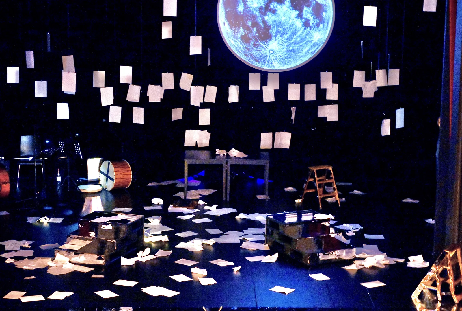 Bühne der Hamburger Kammerspiele mit hängenden Manuskriptseiten und einem Vollmond in der Projektion