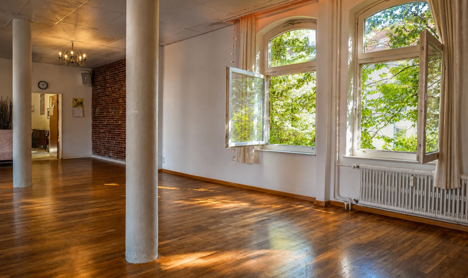 Probenraum am Artrium mit Holzdielen, weißen Säulen, Backsteinwand und geöffneten Bogenfenstern ins Grüne