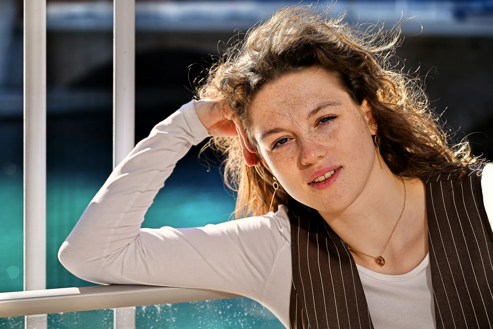 Junge Schauspielerin lehnt entspannt an einem Geländer am Wasser und schaut in die Kamera