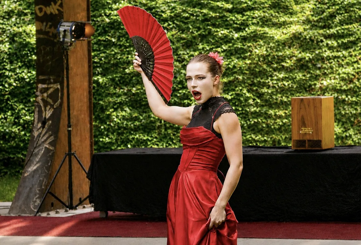 Darstellerin der Sommerakademie im roten Kleid mit Fächer bei einer Flamenco-Szene auf der Outdoorbühne