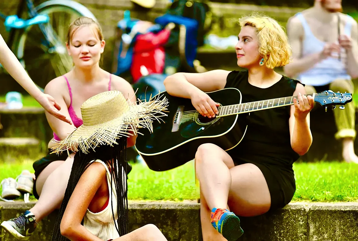 Zwei Teilnehmerinnen der Sommerakademie musizieren mit Gitarre und Sonnenhut im Park
